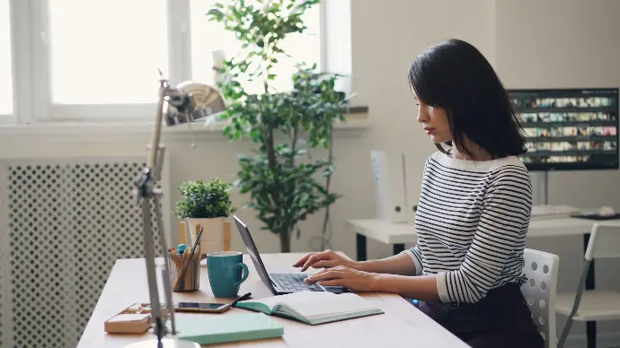 a woman sitting at a desk using a laptop computer, analyse